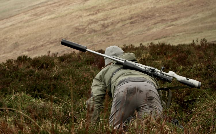 A deer stalker on his hands and knees with a rifle on his back 